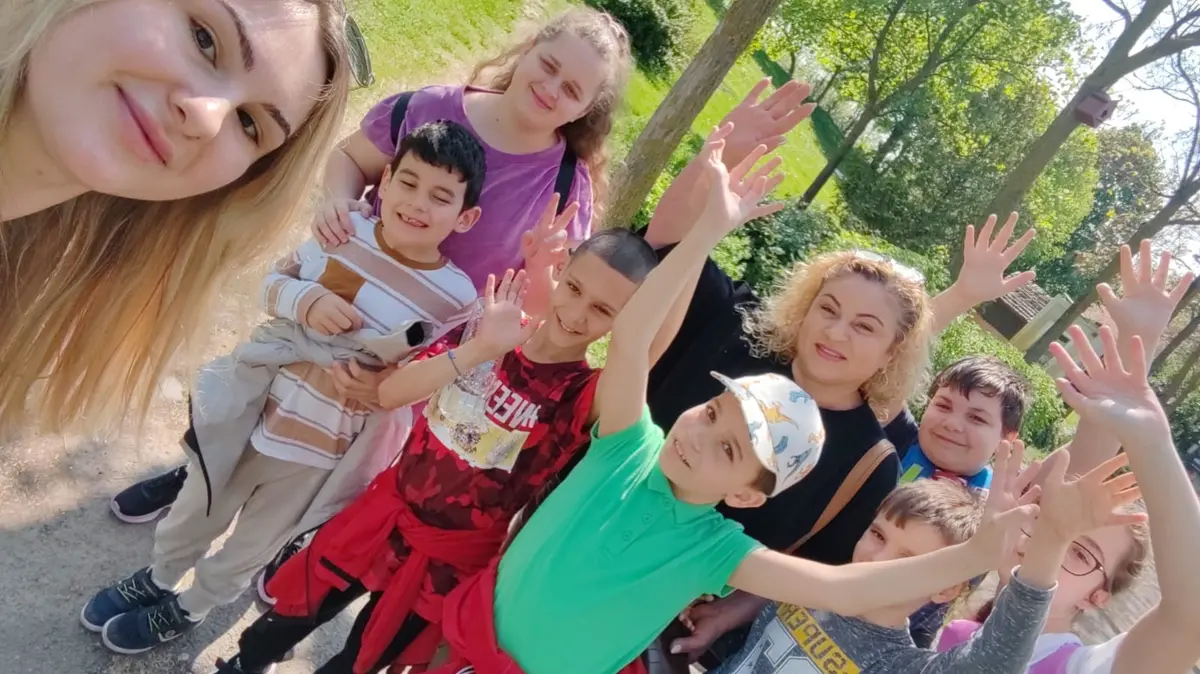 Copii și voluntari în parc, cu mâinile ridicate, veseli