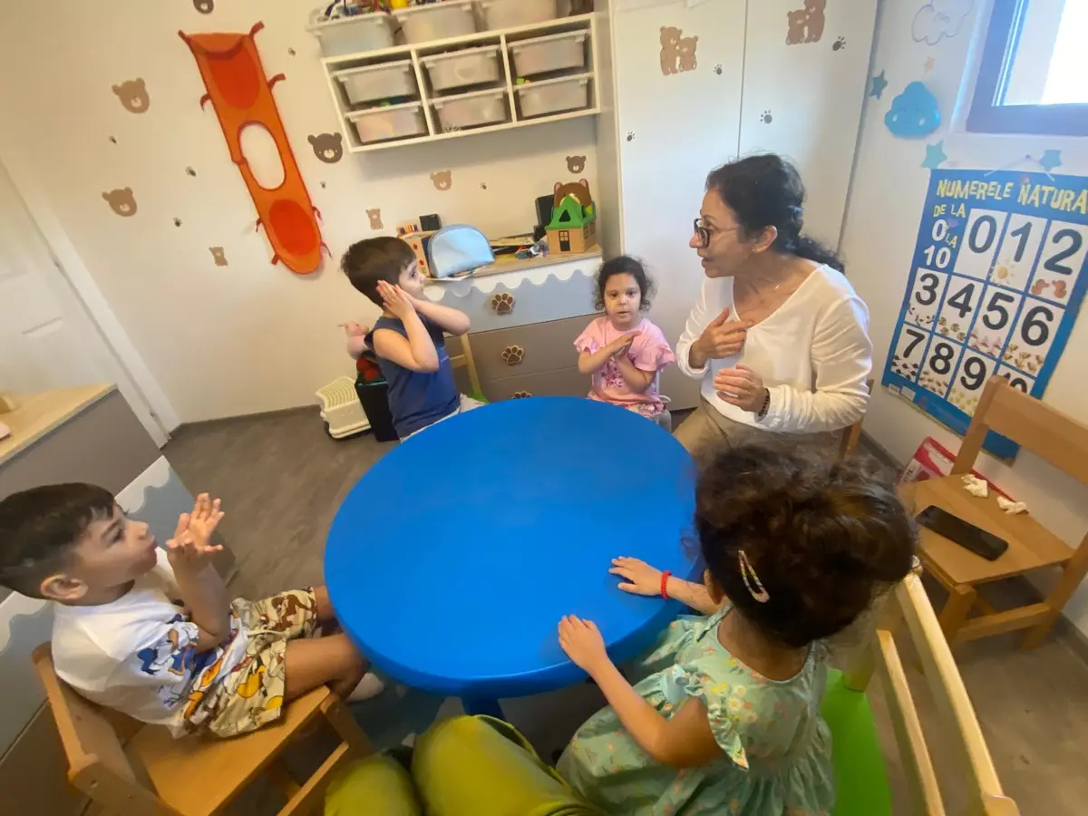 O educatoare și mai mulți copii la masa albastră, bucurându-se împreună