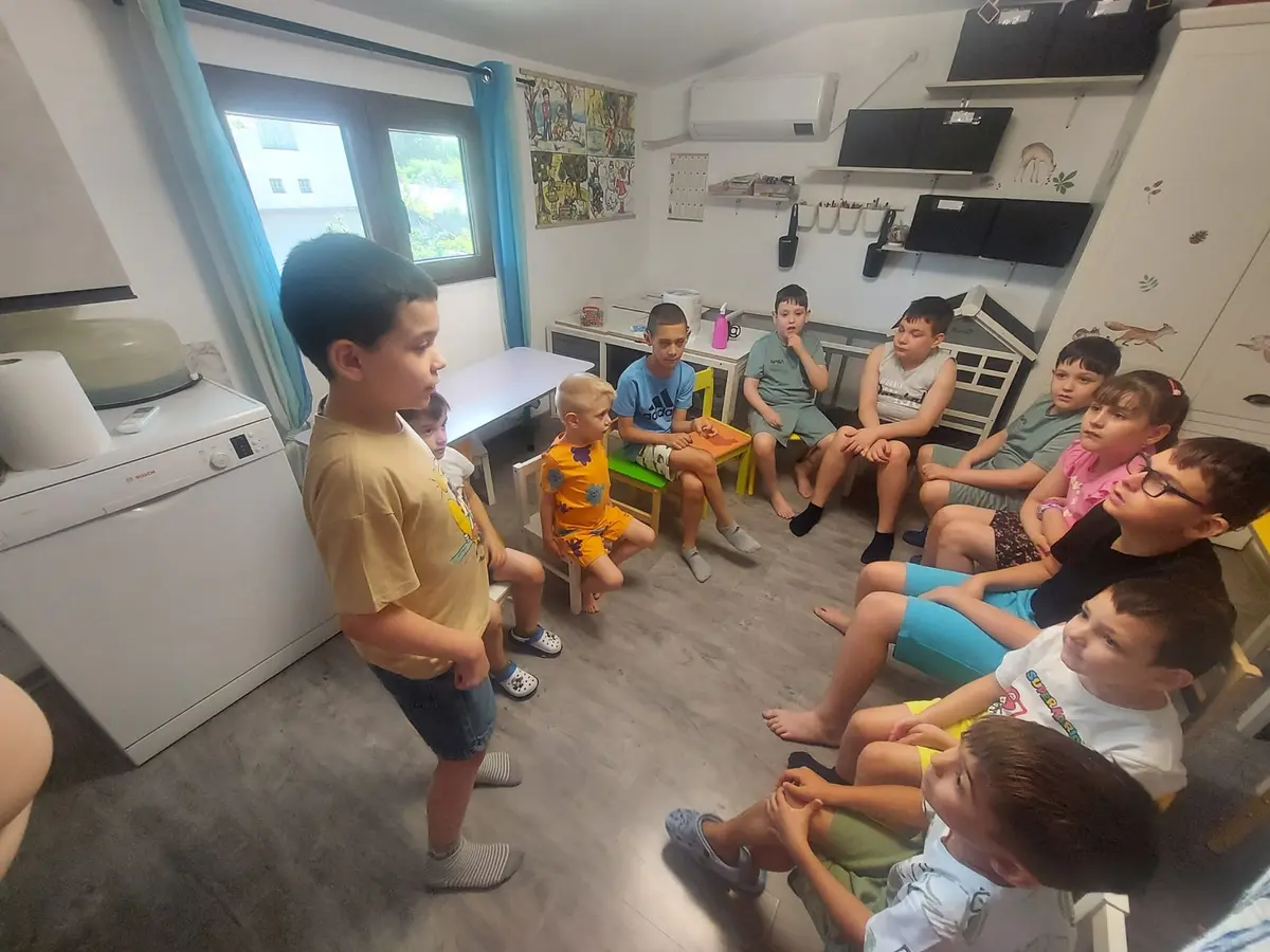 Un cerc mare de copii, un băiat în picioare povestind celorlalți